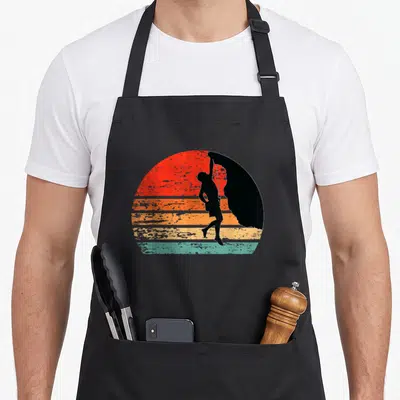 Rock climber apron - Black paraglider silhouette on retro red orange yellow and teal striped sun — shown on a black cotton canvas apron against a white background