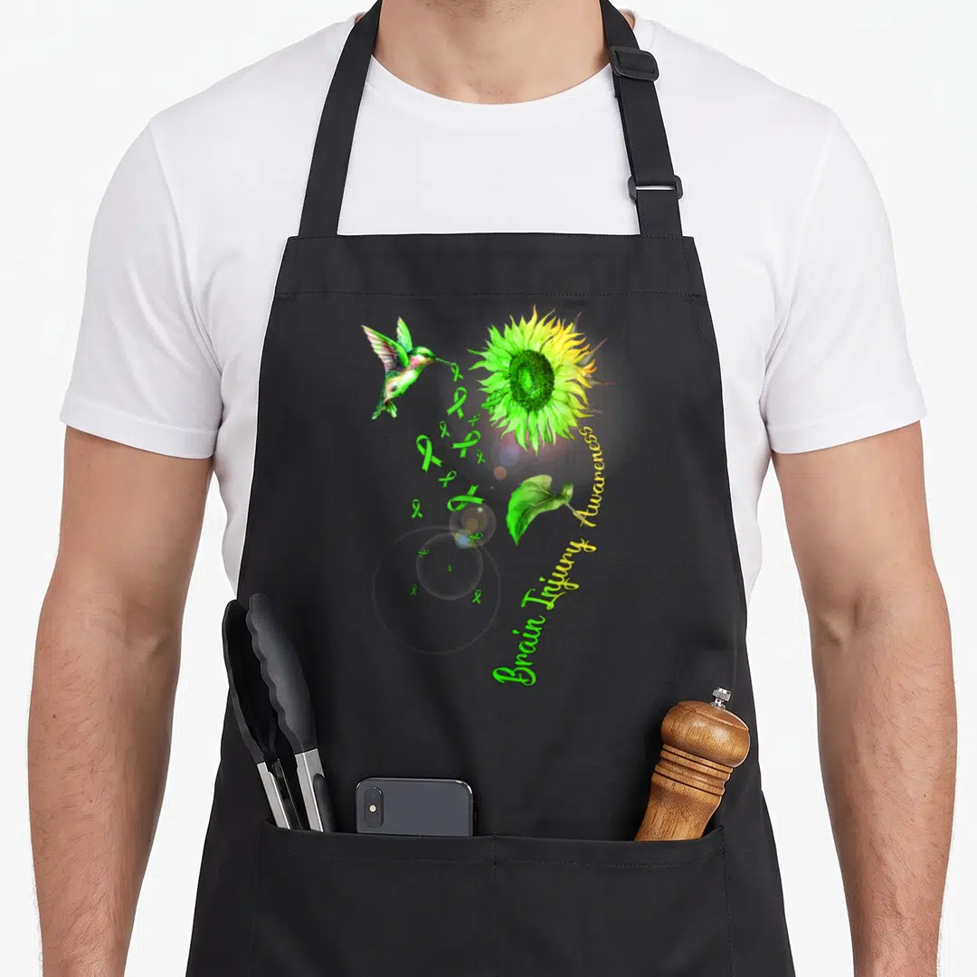 Brain sunflower apron - Hummingbird carrying green ribbons near yellow sunflower with awareness text — shown on a black cotton canvas apron against a white background