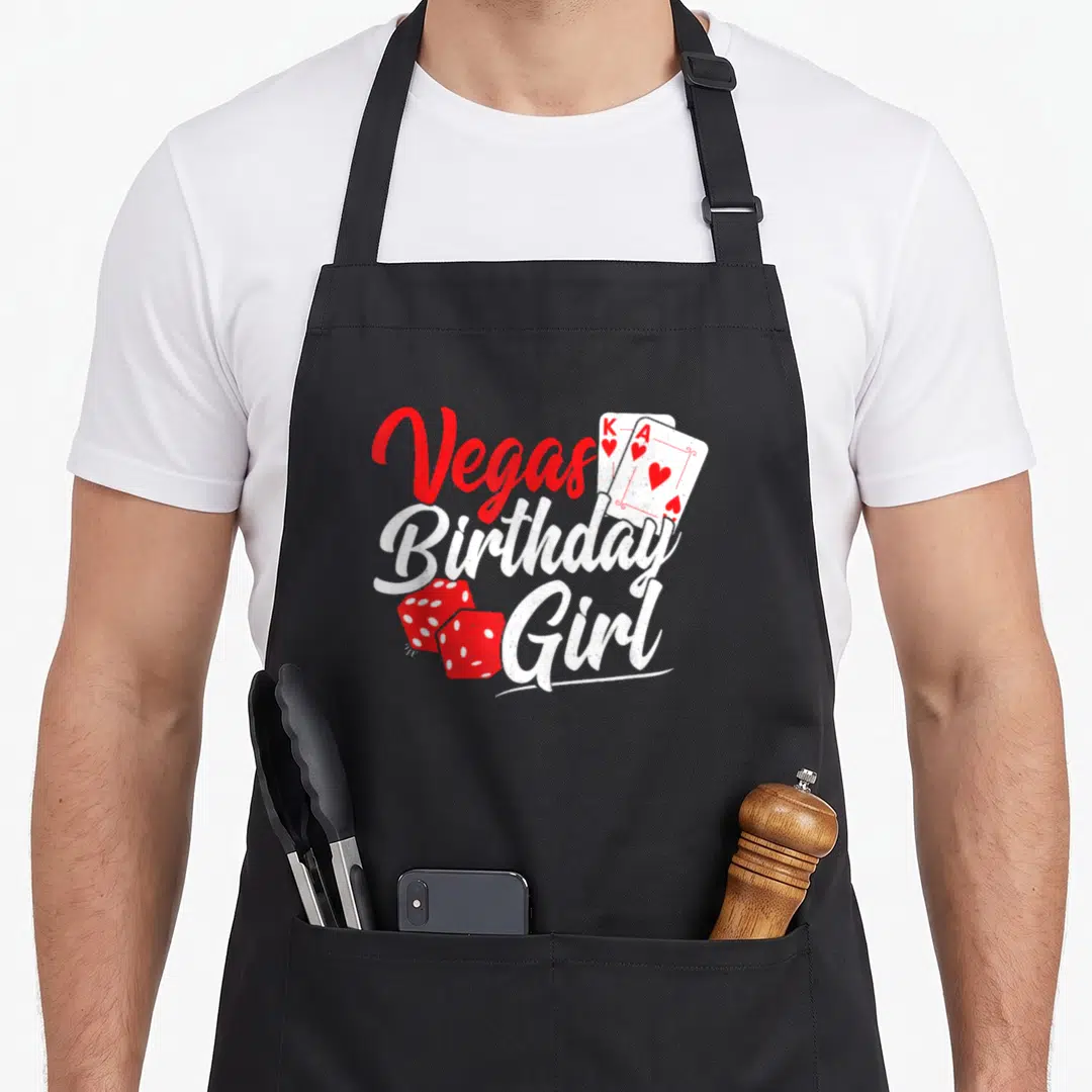 Vegas squad birthday apron - Red and white stacked text reading Vegas Birthday Girl with playing cards and dice — shown on a black cotton canvas apron against a white background