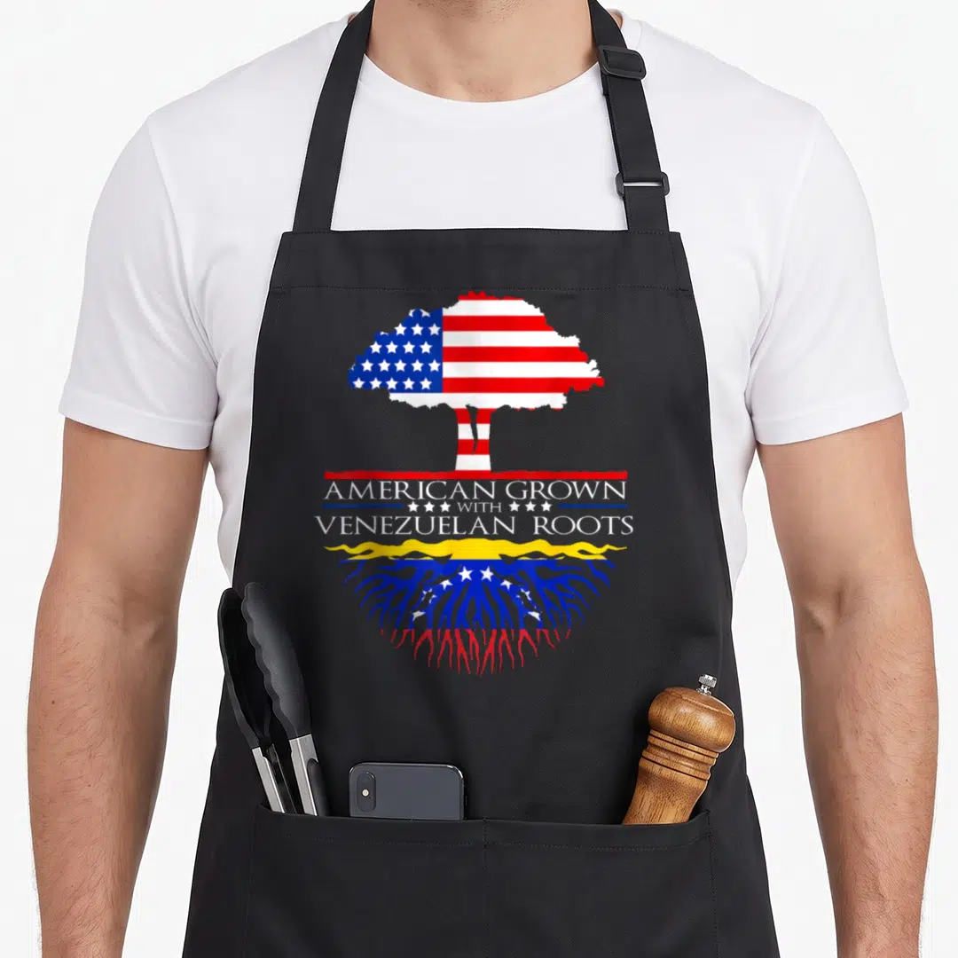 Root grown american flag apron - Tree with American flag canopy and Venezuelan roots displaying AMERICAN GROWN — shown on a black cotton canvas apron against a white background