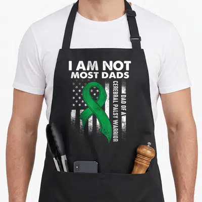 Most cerebral palsy awareness apron - Green ribbon on distressed white flag with text I AM NOT MOST DADS — shown on a black cotton canvas apron against a white background