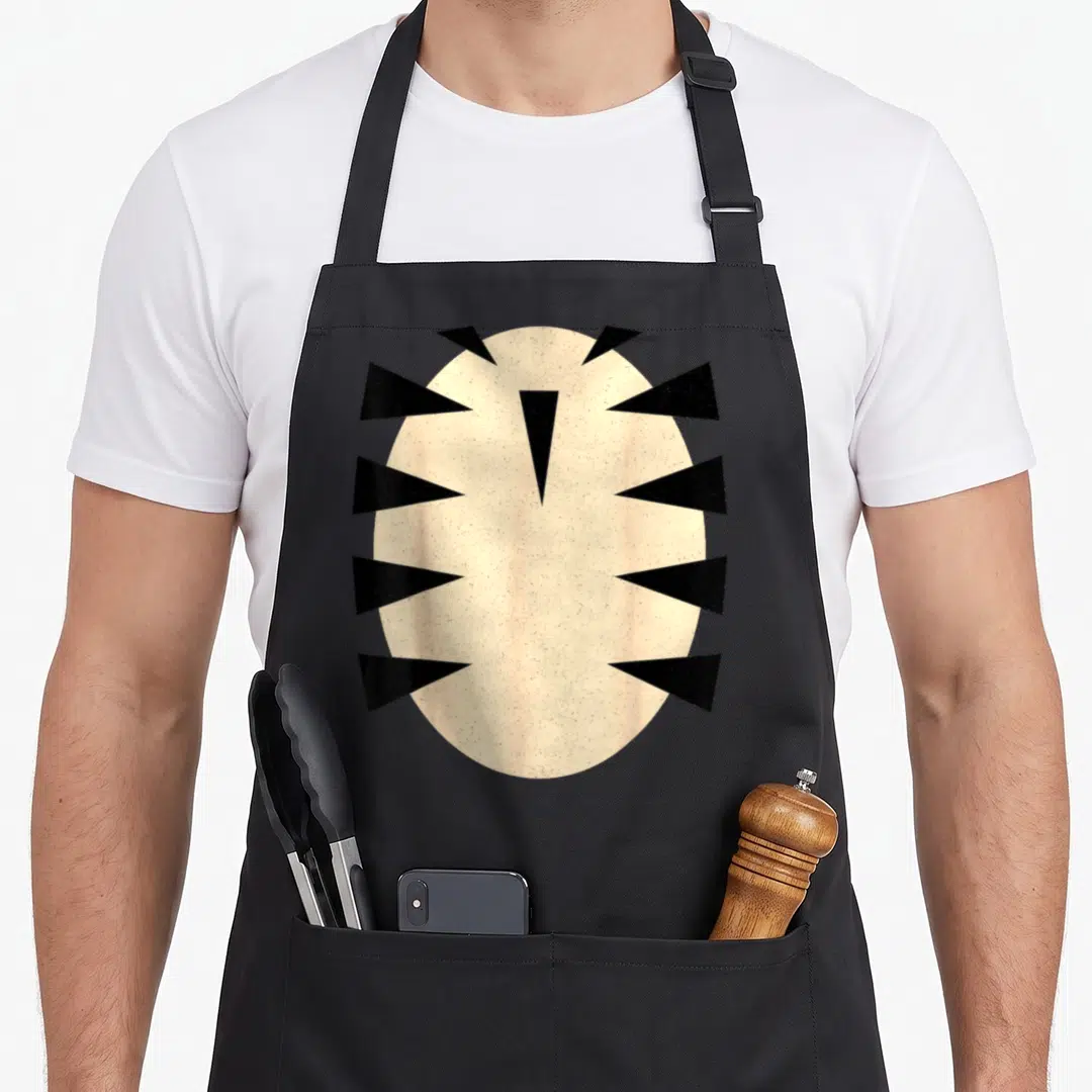 Costume tiger apron - Beige oval surrounded by black triangles pointing inward on grey background — shown on a black cotton canvas apron against a white background