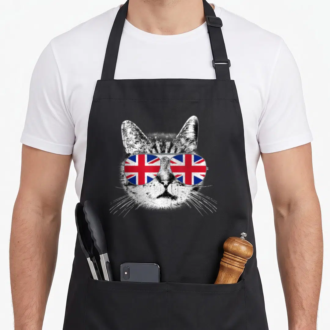 English union jack apron - Tabby cat face wearing aviator sunglasses with Union Jack flag pattern on lenses — shown on a black cotton canvas apron against a white background