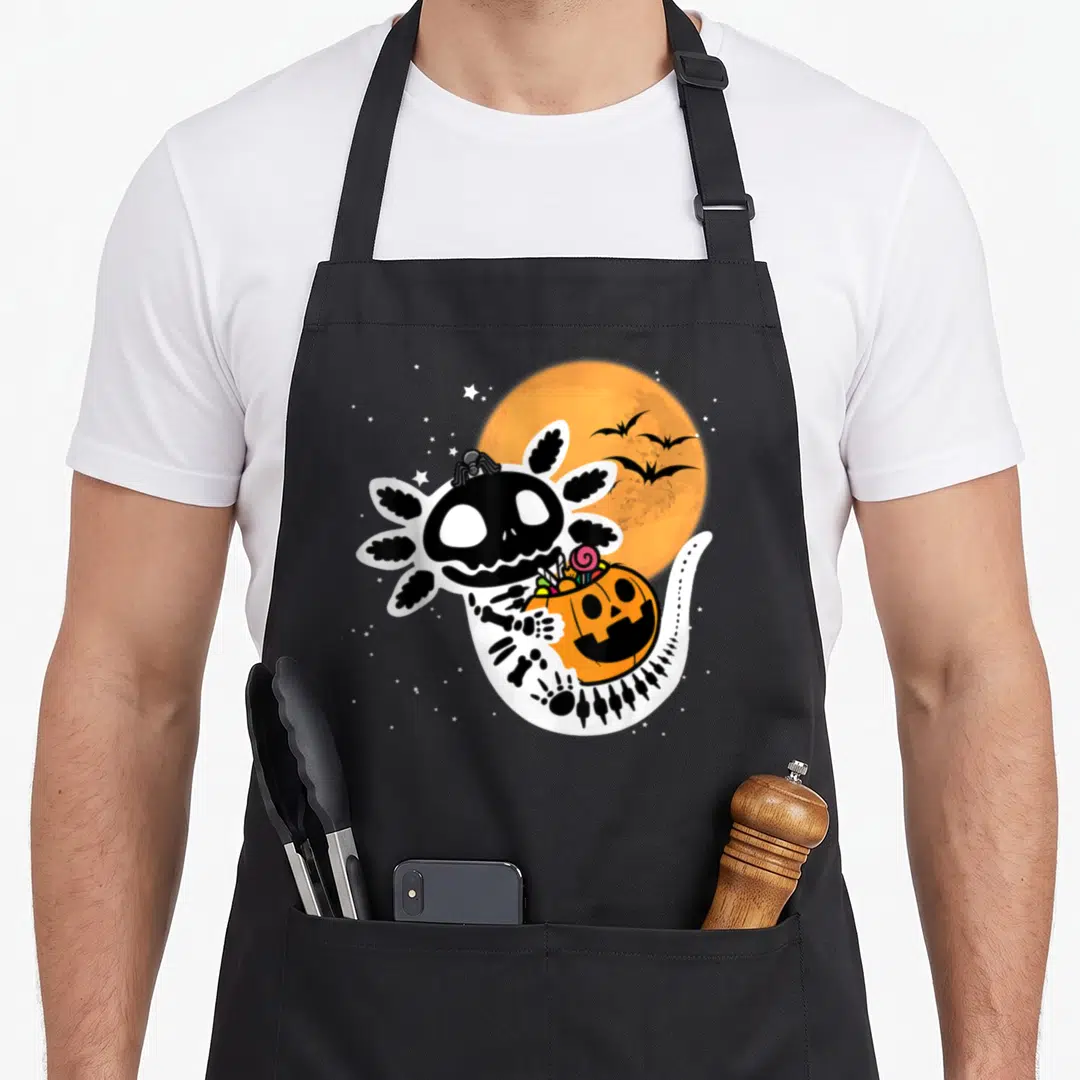 Axolotl halloween apron - Skeleton axolotl holding orange candy pumpkin under moon with bats and stars — shown on a black cotton canvas apron against a white background