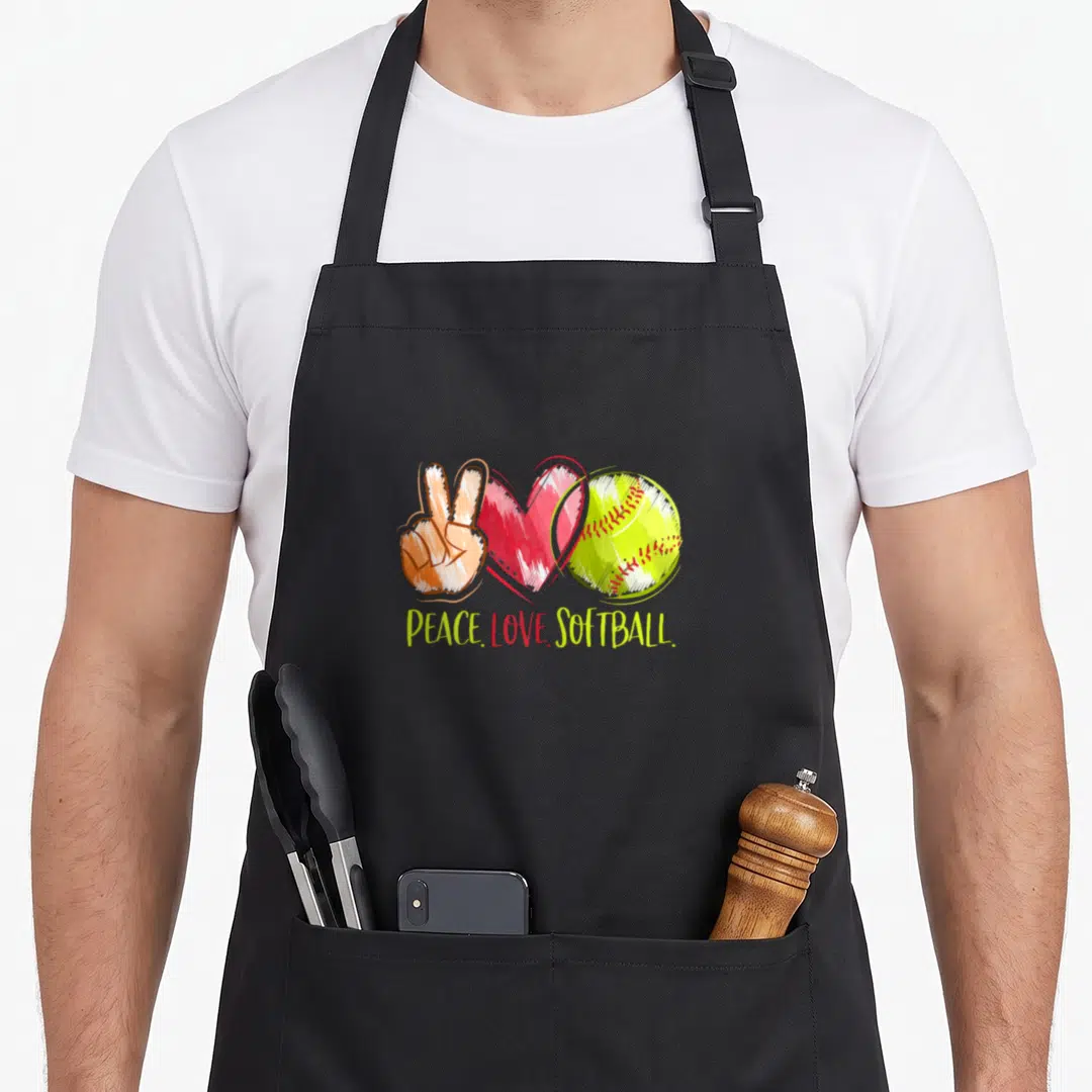 Player i love softball apron - Cartoon peace sign, red heart, and yellow softball with PEACE LOVE SOFTBALL text — shown on a black cotton canvas apron against a white background