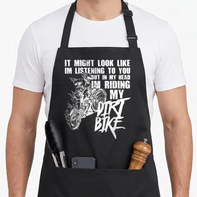 Riding dirt bike apron - White line art of a dirt bike rider with text about being mentally riding instead of listening — shown on a black cotton canvas apron against a white background