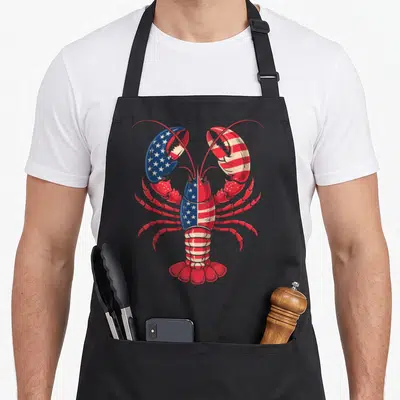 Flag lobster apron - Cartoon lobster with red white and blue flag pattern on left claw center body and tail — shown on a black cotton canvas apron against a white background