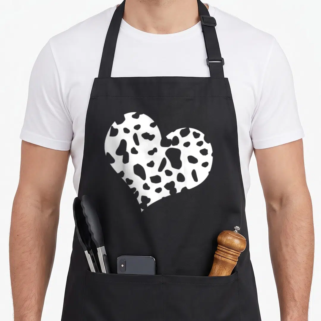 Funny dalmatian apron - White heart shape filled with grey Dalmatian spots on a black background — shown on a black cotton canvas apron against a white background