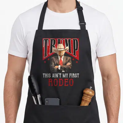 Trump western aprons - Donald Trump cowboy hat graphic with red stars and text THIS AIN'T MY FIRST RODEO — shown on a black cotton canvas apron against a white background