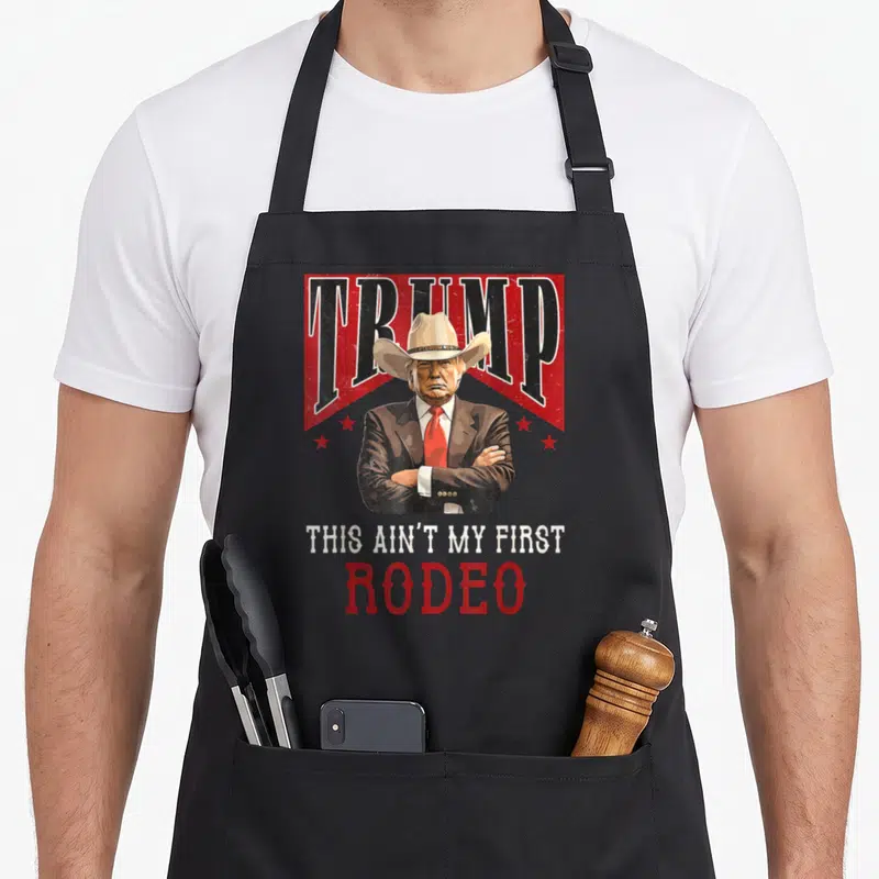 Trump western aprons - Donald Trump cowboy hat graphic with red stars and text THIS AIN'T MY FIRST RODEO — shown on a black cotton canvas apron against a white background