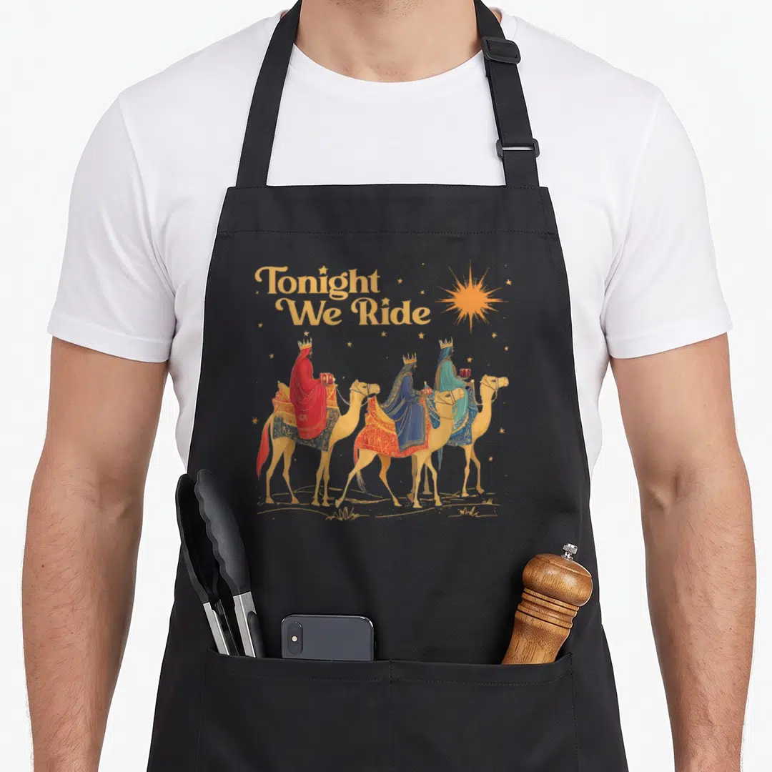 Wise christmas apron - Three wise men riding camels under Tonight We Ride text with a gold star — shown on a black cotton canvas apron against a white background