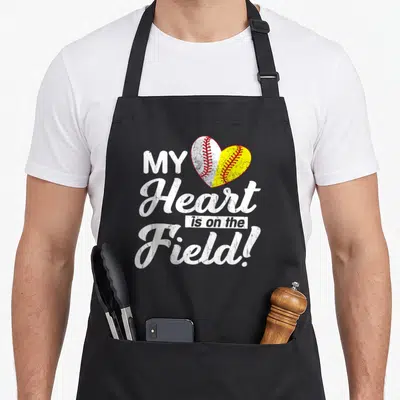 Field baseball mother's day aprons - Split heart baseball softball graphic with distressed white and yellow text — shown on a black cotton canvas apron against a white background