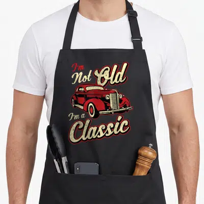 Fan car apron - Red vintage car with I'm Not Old I'm a Classic text in retro style — shown on a black cotton canvas apron against a white background
