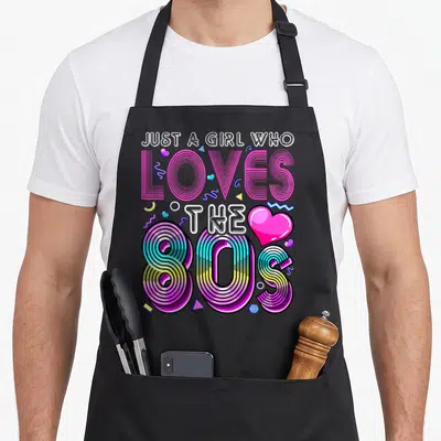 Retro costume 80s apron - Stacked text Just a Girl Who Loves the 80S with striped retro typography and scattered — shown on a black cotton canvas apron against a white background