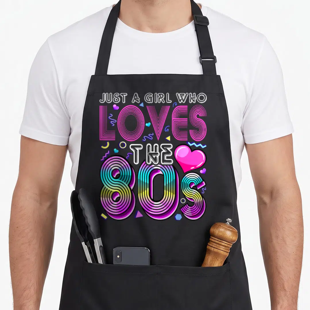 Retro costume 80s apron - Stacked text Just a Girl Who Loves the 80S with striped retro typography and scattered — shown on a black cotton canvas apron against a white background