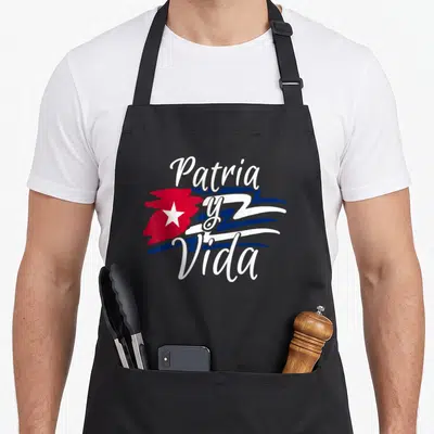 Cuban cuba libre apron - Patria y Vida white script over red island star and blue stripes cartoon art — shown on a black cotton canvas apron against a white background