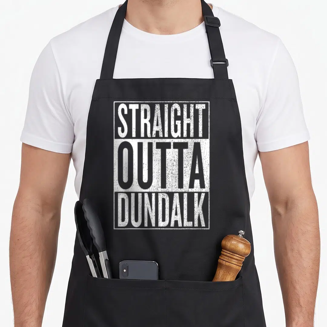 Straight chef outfit with apron - White distressed text reading straight outta dundalk stacked in three lines inside — shown on a black cotton canvas apron against a white background