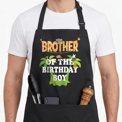 Brother zoo birthday apron - Cartoon animals perched on orange zebra-print text reading Brother Of The Birthday Boy — shown on a black cotton canvas apron against a white background