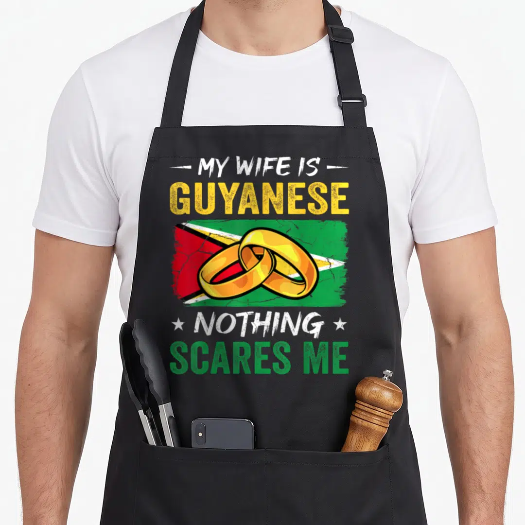Guyanese husband wife aprons - My Wife Is Guyanese text with two interlocking gold rings on a distressed green yellow — shown on a black cotton canvas apron against a white background