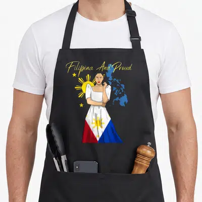 Pinay filipino apron - Woman in flag-patterned dress with arched yellow text and blue map silhouette — shown on a black cotton canvas apron against a white background
