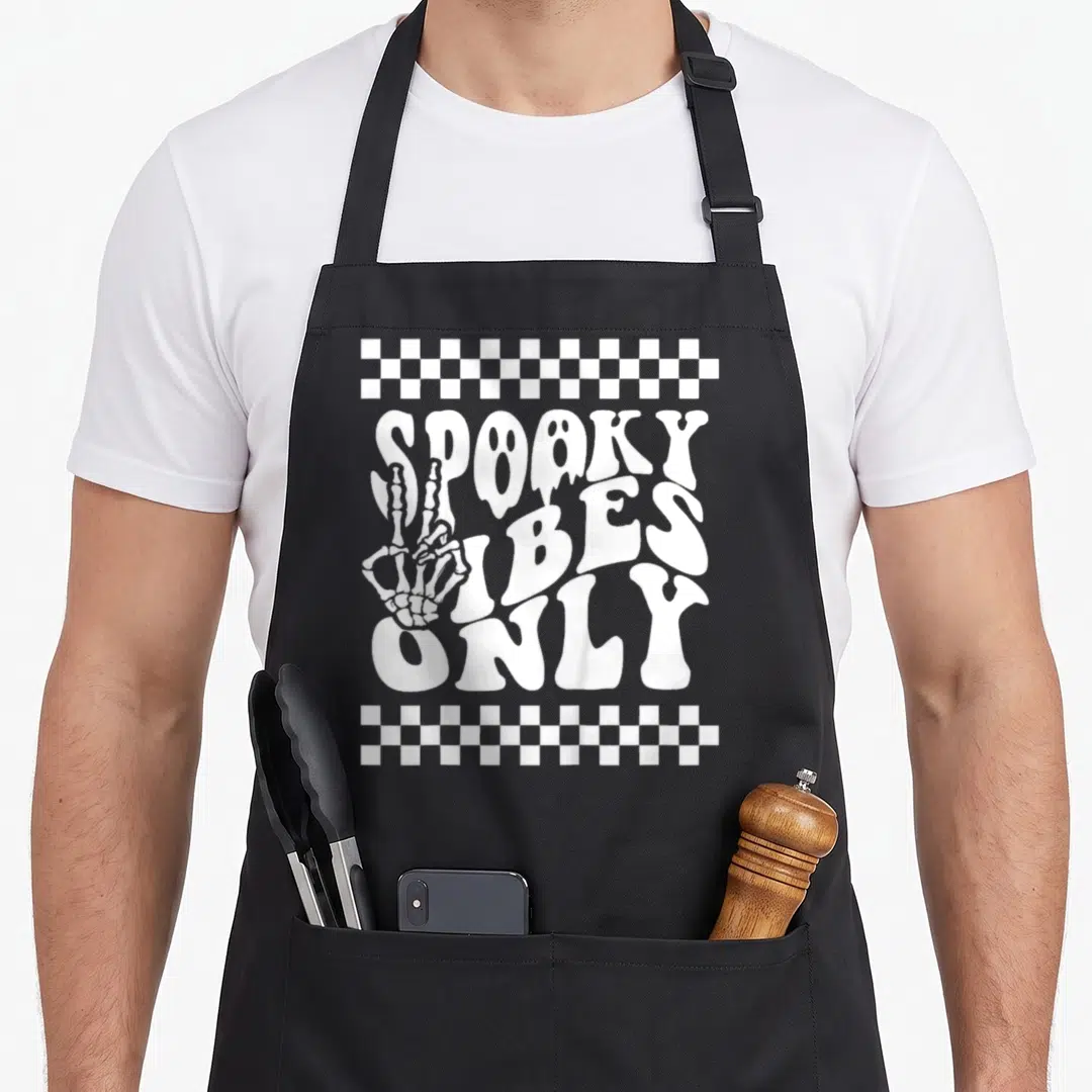 Toddler spooky apron - White skeleton hand holding peace sign next to stacked SPOOKY VIBES ONLY text with ghost details — shown on a black cotton canvas apron against a white background