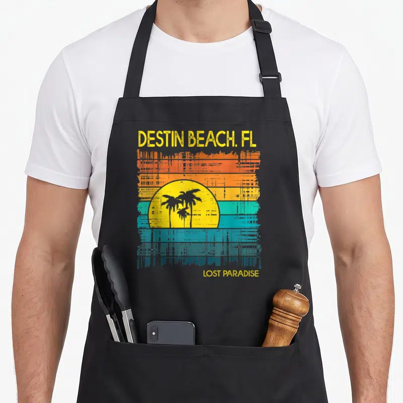 Beach sunset florida apron - DESTIN BEACH FL LOST PARADISE text above distressed sunset with yellow sun and palm trees — shown on a black cotton canvas apron against a white background
