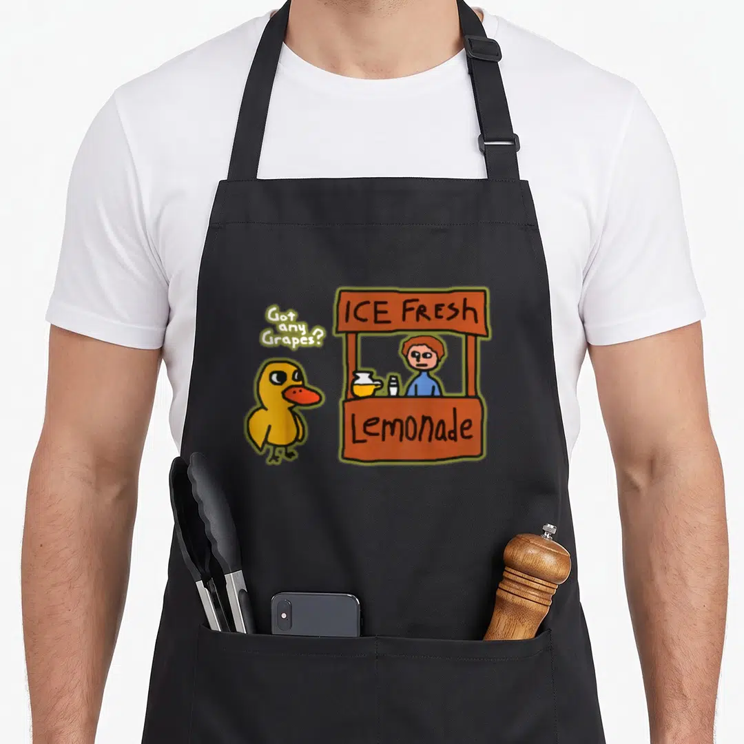 Ice duck apron - Cartoon yellow duck asking Got any Grapes near Ice Fresh Lemonade stand — shown on a black cotton canvas apron against a white background