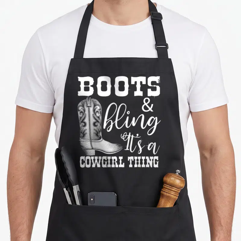 Cowgirl country apron - White cowboy boot with BOOTS & bling It's a COWGIRL THING text in western fonts — shown on a black cotton canvas apron against a white background