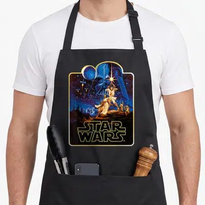 Hope wars new apron - Retro Star Wars poster art with Vader helmet, Luke, Leia, Death Star, and TIE fighters — shown on a black cotton canvas apron against a white background