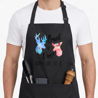 Funny boho apron - Blue buck and pink doe watercolor silhouettes with floral crown and gender reveal text — shown on a black cotton canvas apron against a white background