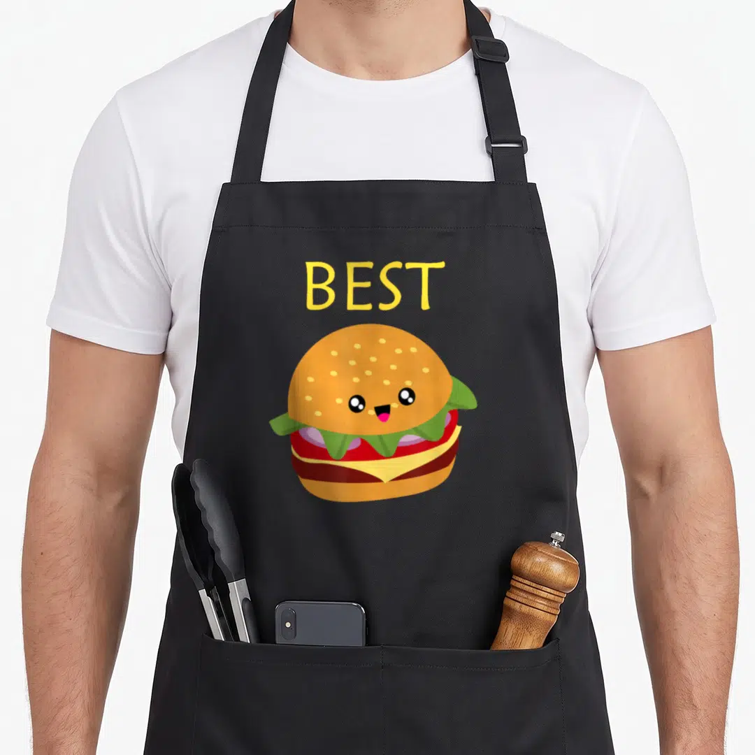 Burger fry apron - Yellow BEST text above cute cartoon hamburger with orange bun, green lettuce, red tomato, brown — shown on a black cotton canvas apron against a white background