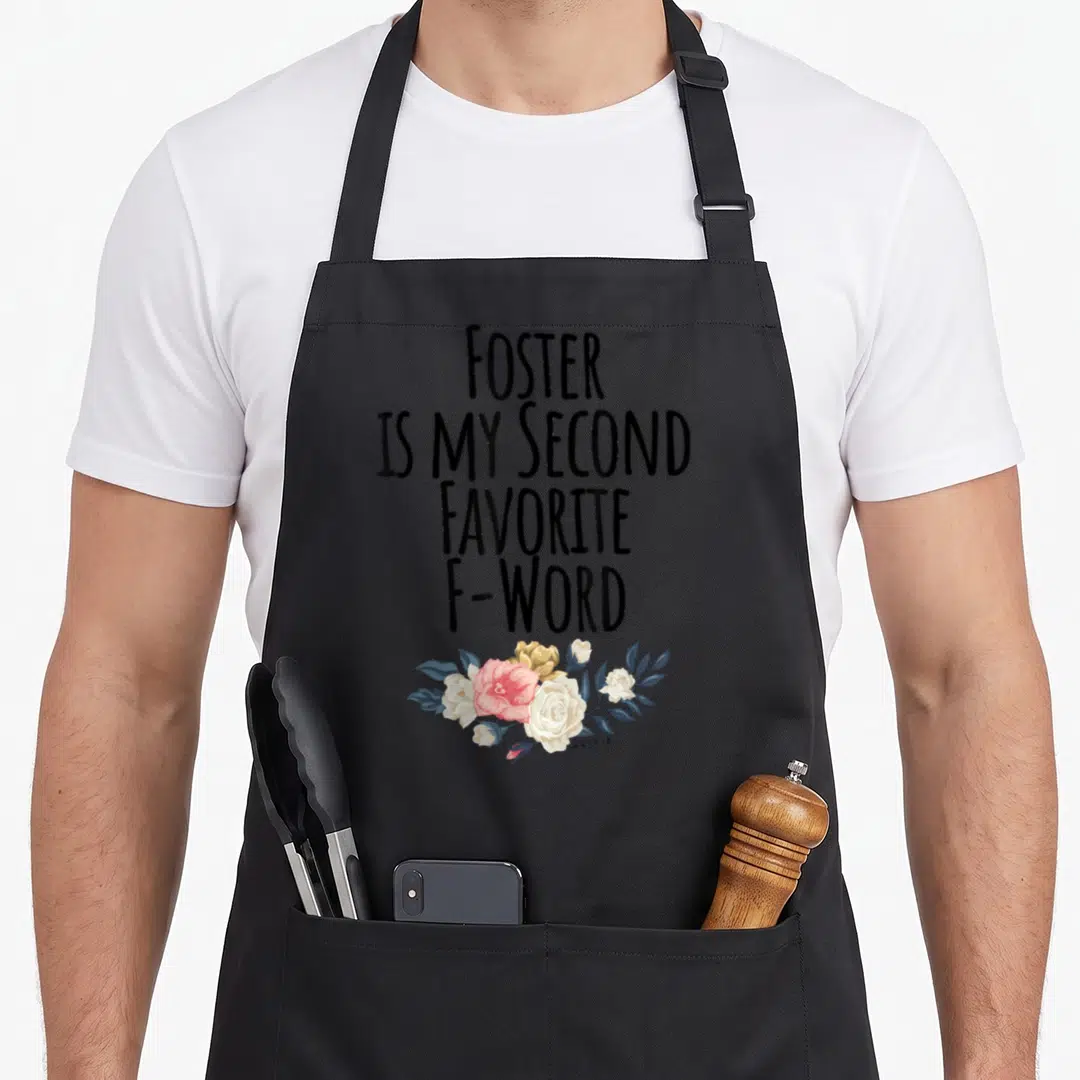 Foster dog mom apron - Stacked black text reading Foster Is My Second Favorite F-Word above pink white and blue-grey — shown on a black cotton canvas apron against a white background