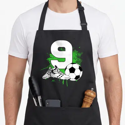 Football birthday apron - Number 9, soccer ball, two cleats, green splatter — shown on a black cotton canvas apron against a white background