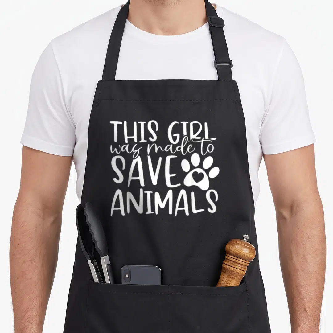 Assistant vet apron - White stacked text This Girl was made to Save Animals next to paw print with heart inside main pad — shown on a black cotton canvas apron against a white background