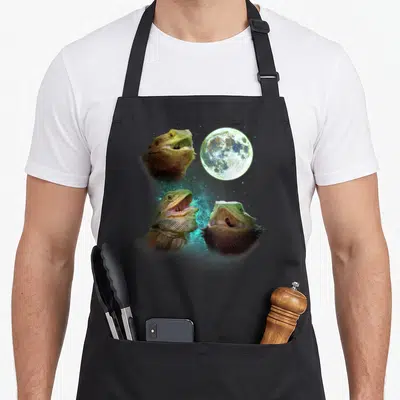 Three dragon apron - Three bearded dragon heads with open mouths around a teal nebula and moon — shown on a black cotton canvas apron against a white background