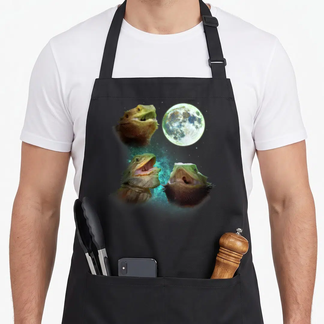 Three dragon apron - Three bearded dragon heads with open mouths around a teal nebula and moon — shown on a black cotton canvas apron against a white background