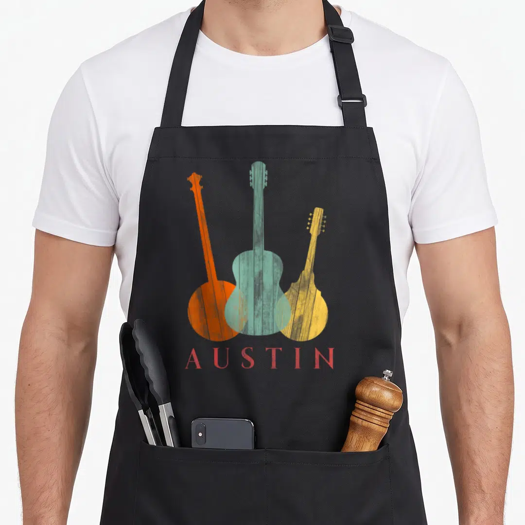 Distressed texas aprons - Three retro banjo, guitar, mandolin in orange teal yellow with AUSTIN text — shown on a black cotton canvas apron against a white background