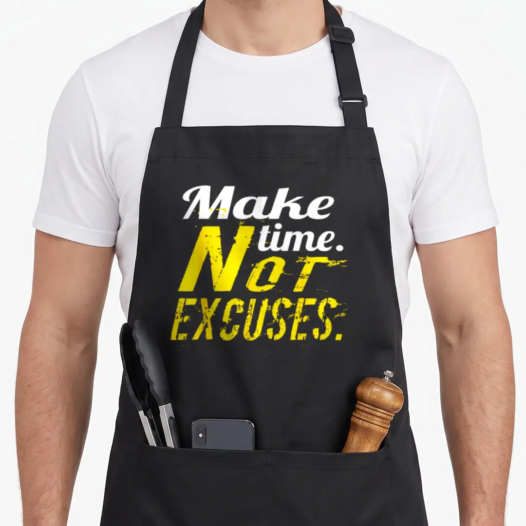 Excuse bodybuilding apron - Stacked white and yellow distressed typography reading Make time Not Excuses — shown on a black cotton canvas apron against a white background