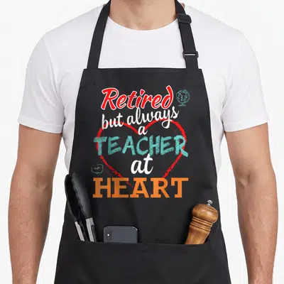 Alway teachers apron - Red heart outline with teal TEACHER text, globe, and 1+2 math bubble — shown on a black cotton canvas apron against a white background