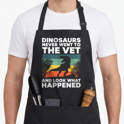 Funny veterinarian veterinary apron - Dinosaur silhouette on colored stripes with text about never going to the vet — shown on a black cotton canvas apron against a white background