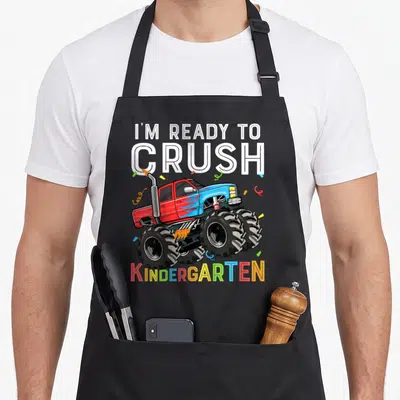 Occasion truck apron - Cartoon monster truck in red and blue surrounded by confetti with I'm Ready to Crush — shown on a black cotton canvas apron against a white background
