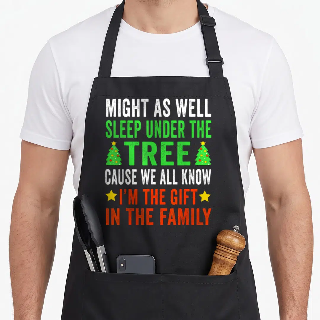 Pajamas christmas apron - Distressed text reading Sleep Under The Tree with two small Christmas trees and yellow stars — shown on a black cotton canvas apron against a white background