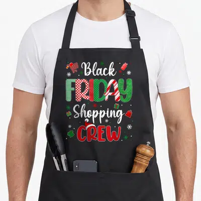 Christmas shopping black friday apron - Stacked Black FRIDAY Shopping CREW text with Santa hat and festive icons in red — shown on a black cotton canvas apron against a white background