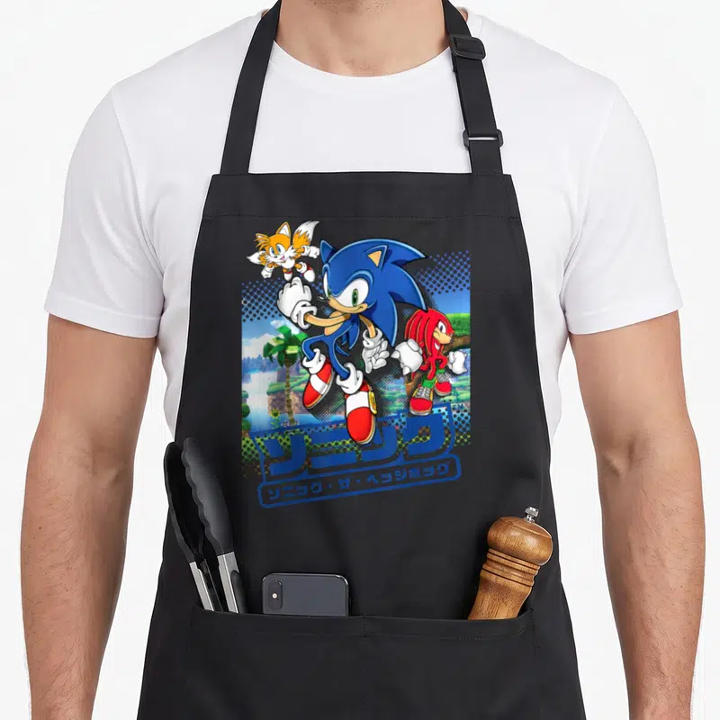 Funny friends apron - Sonic Tails and Knuckles running with Japanese text and tropical background — shown on a black cotton canvas apron against a white background