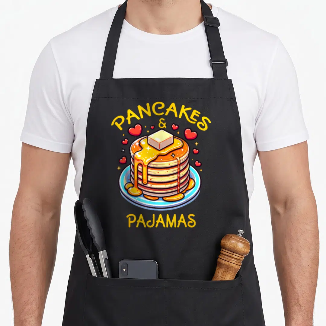 Adorable pancake apron - Cartoon stack of pancakes with butter on blue plate and PANCAKES & PAJAMAS text surrounded — shown on a black cotton canvas apron against a white background