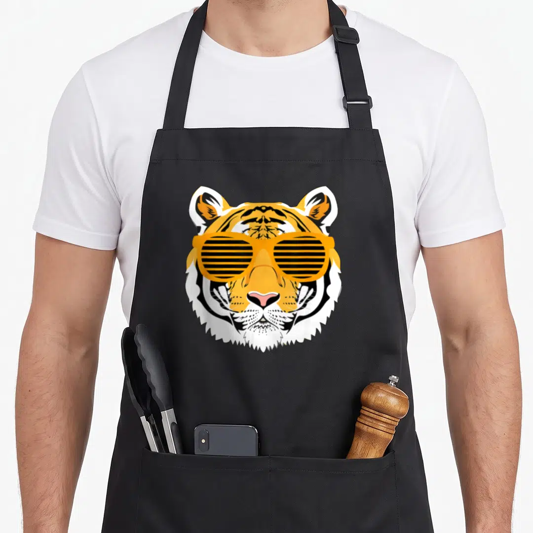 Tiger animal apron - Cartoon tiger head wearing orange shutter shades in black and white — shown on a black cotton canvas apron against a white background