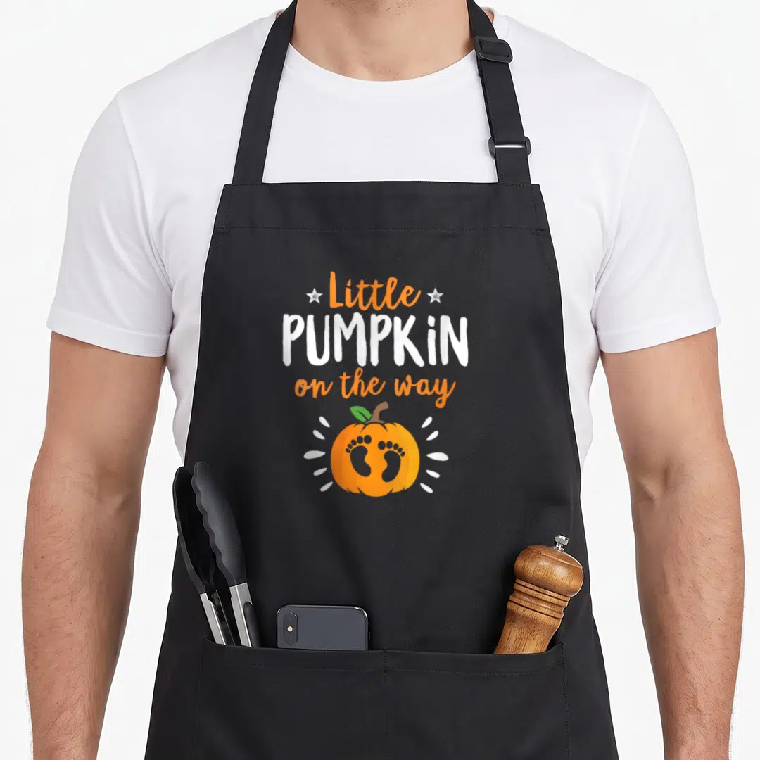Way pumpkin apron - Little PUMPKIN on the way text above orange pumpkin with footprints and stars — shown on a black cotton canvas apron against a white background