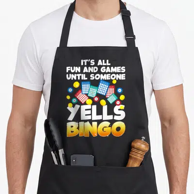 Gambling player bingo apron - Scattered bingo cards and balls with It's All Fun and Games Until Someone Yells Bingo text — shown on a black cotton canvas apron against a white background