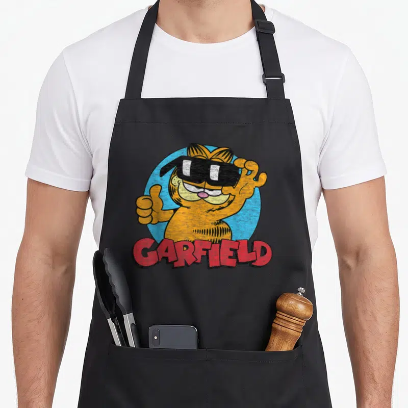 Sunglass cat apron - Orange Garfield cat wearing black sunglasses giving thumbs up in blue circle with red text — shown on a black cotton canvas apron against a white background