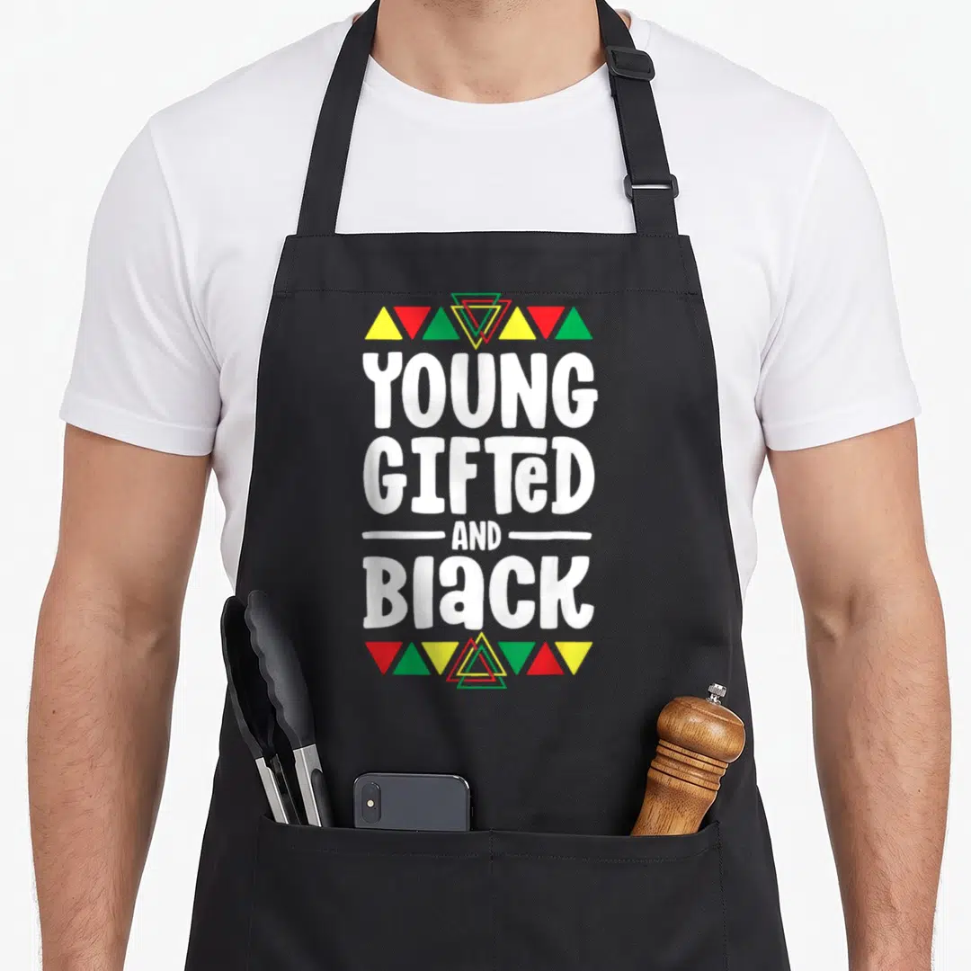 Young african apron - White Young Gifted And Black text framed by red yellow green triangles on black fabric — shown on a black cotton canvas apron against a white background